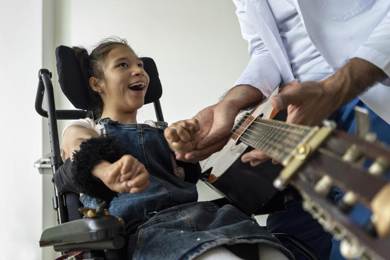 Disabled girl in wheelchair performing music therapy 