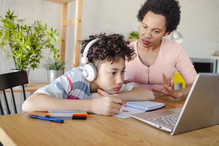 Teenager wearing headphones using a computer at a dining room with another adult